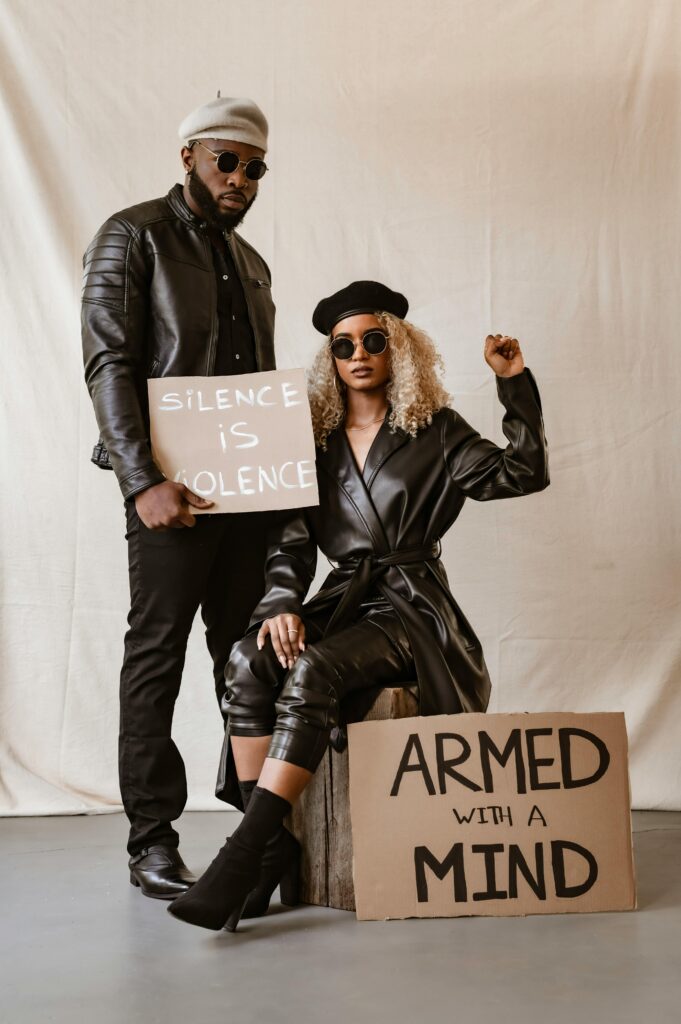 Two adults in leather outfits express activism through protest signs.